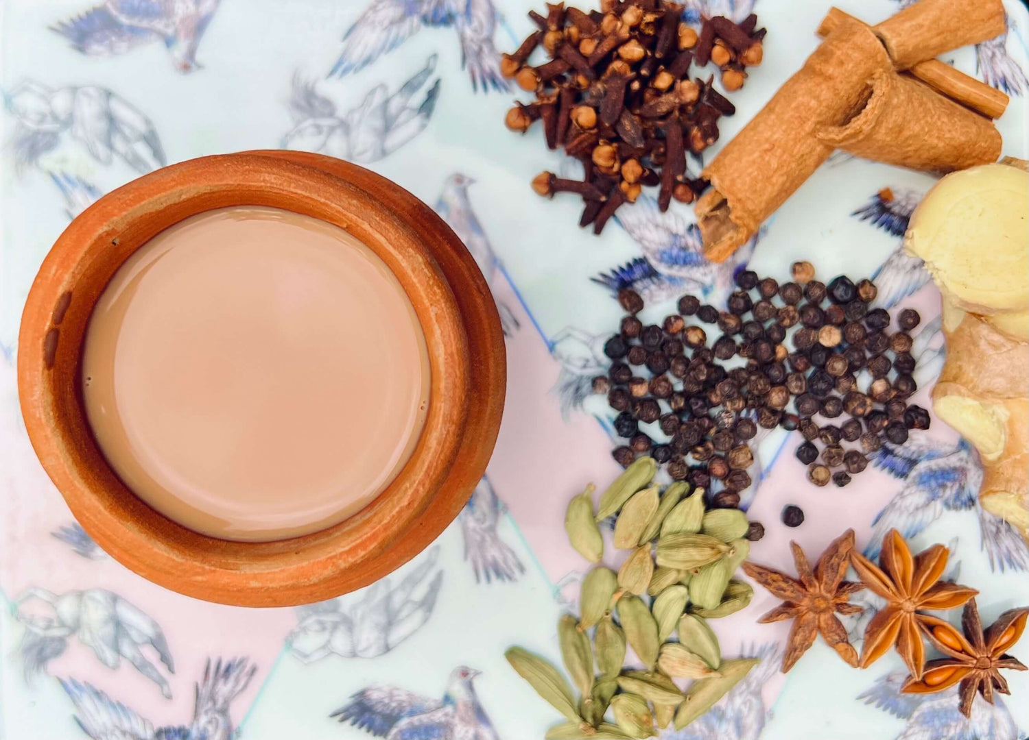 A traditional clay cup filled with instant chai latte, surrounded by spices for masala chai mix, including cardamom and ginger.